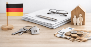 Nachfolgeplanung visualisiert durch Vertragsdokumente, Hausschlüssel, Euro-Banknoten und Münzen sowie Familienfiguren und deutsche Flagge als Symbol für Vermögensübertragung und finanzielle Planung für Investoren.