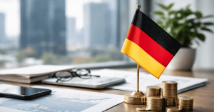 Deutsche Flagge auf einem Schreibtisch neben gestapelten Münzen, Finanzdokumenten und Diagrammen, die Investitionen und Vermögensaufbau in Deutschland symbolisieren. Im Hintergrund sind moderne Bürogebäude zu sehen, während Smartphone und Brille auf dem Tisch liegen. Das Bild steht für Finanzplanung, Kapitalanlage und wirtschaftliches Wachstum auf dem deutschen Markt.